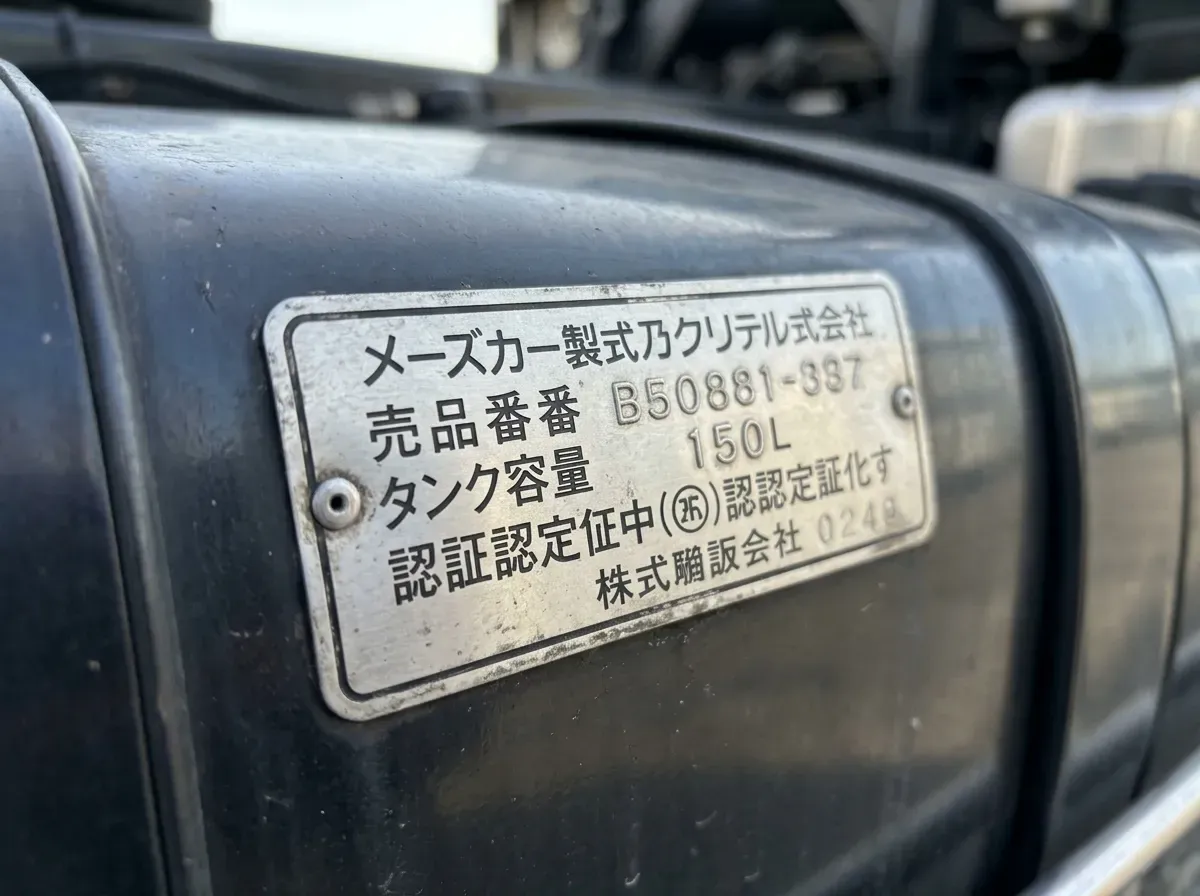 トラック燃料タンクの表面に貼られた金属製銘板(シール)の拡大写真。品番・容量・認証マークが刻印されており、適合品を探す際に確認すべき箇所を示す。